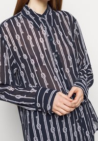 Camicia trasparente blu navy con motivo a corda bianca, caratterizzata da una chiusura frontale a bottoni e maniche lunghe con polsini a contrasto.