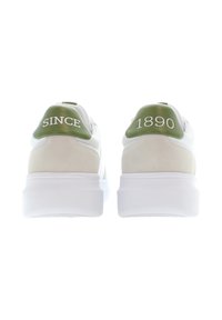 Ett par vita sneakers med gröna hälflikar, en märkt "SINCE" och den andra "1890", visade från baksidan på vit bakgrund.