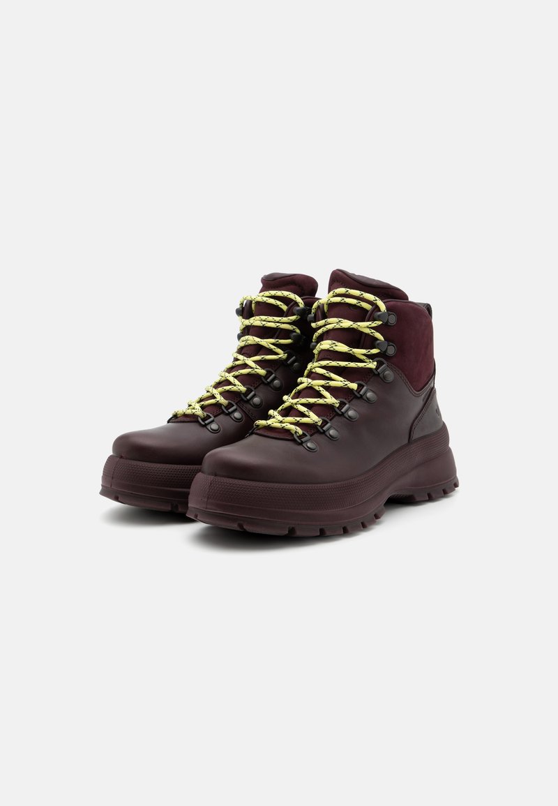Bordeauxkleurige wandelschoenen met gele veters, voorzien van een hoge kraag, rubberen zool en metalen oogjes voor een veilige sluiting. Glad en gestructureerd oppervlak.