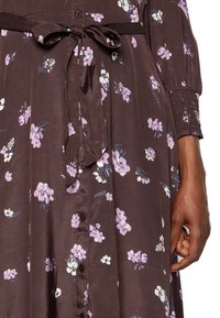 Braun geblümtes Kleid mit lila und weißen Blumen. Satiner Optik mit langen Ärmeln, Knopfverschluss und einer gebundenen Taillendetail.
