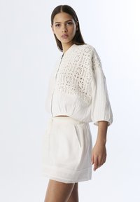 Veste bomber blanche courte avec détail en tricot texturé et fermeture à zip, accompagnée d'une mini jupe légère à cordon de serrage assortie.