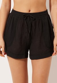 Black shorts made of lightweight fabric with an elastic waistband, drawstring detail, side pockets, and a relaxed fit.