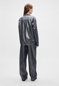 Jaqueta de jeans escuro metálico com um ajuste descontraído, apresentando um yoke traseiro e calças largas combinando, ambas com um brilho suave.