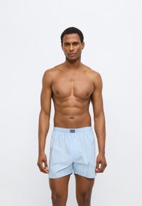 Ανοιχτό μπλε ανδρικά εσώρουχα boxer από μαλακό ύφασμα, με ελαστική μέση και ένα μπροστινό φερμουάρ, παρουσιάζονται σε μοντέλο με ουδέτερο φόντο.