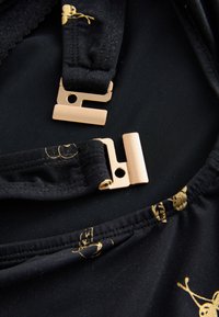 Črna tkanina z gladko teksturo, okrašena z zlatimi vzorci; vsebuje kovinske zaponke in nastavljive trakove.