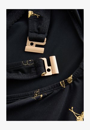 Mustast kangast, millel on sile tekstuur ja kuldsed mustrid; sisaldab metallist riistvara kinnitusi ja reguleeritavaid rihmu.