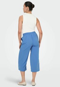 Pantalon bleu clair raccourci avec une taille élastique et des poches latérales, fabriqué dans un tissu doux et respirant. Top blanc sans manches avec une texture côtelée.