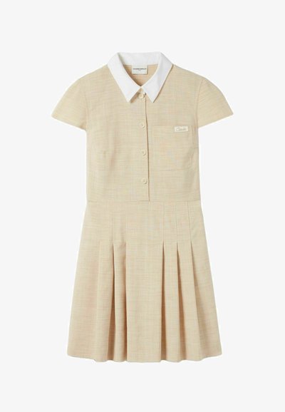 Robe à manches courtes en beige clair avec un col blanc, une fermeture à bouton sur le devant et une poche sur la poitrine. Présente des plis verticaux sur la jupe.