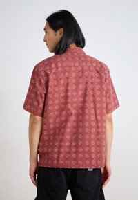 Maglietta a maniche corte in tessuto rosso con un motivo di cuori e punti bianchi. Colletto classico, vestibilità comoda e dettaglio del plissettato sul retro.