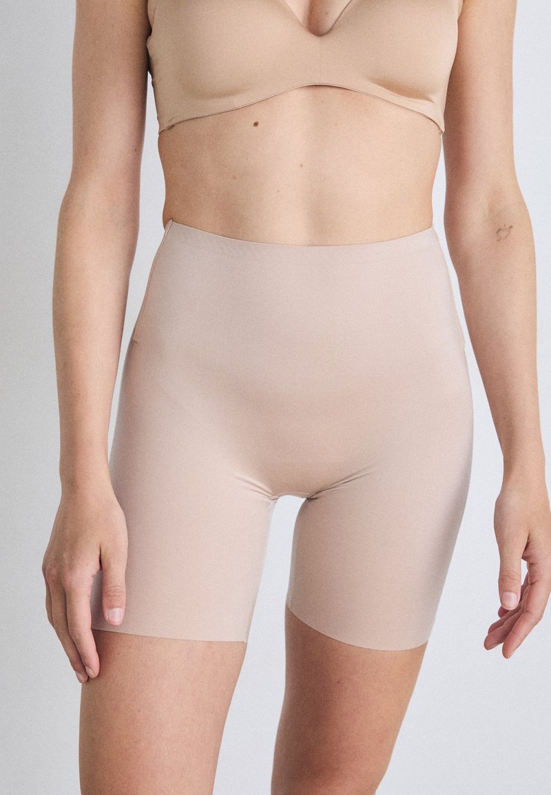 Şorturi modelatoare nude realizate dintr-un material neted și elastic. Design cu talie înaltă și finisaj fără cusături, care se extinde până la jumătatea coapsei.