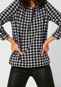 Navy and white gingham pattern top with three-quarter sleeves, featuring a round neckline and side pockets, worn over black pants.