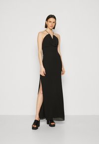 Rochie maxi neagră cu gât halter, corp drapat, fanta laterală și textură fină. Asortată cu pantofi cu toc gros, negru, cu platformă.