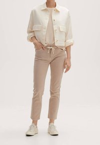 Cream-colored cropped jacket with two front pockets, paired with light beige, drawstring pants and white sneakers. Textured fabric details visible.