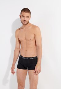 Boxer shorts negros con una cinturilla blanca contrastante, diseño ajustado, tejido suave y estilo minimalista. El modelo muestra una vista frontal.