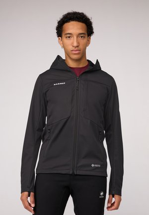 Veste softshell noire avec capuche, dotée de poches zippées, d'une texture lisse et d'un design ajusté. Marquage sur la poitrine et l'ourlet inférieur.