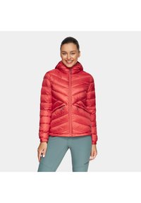 Czerwona pikowana kurtka z kapturem, z wzorem w zygzak, z zapięciem na zamek i szczegółami ze sznurkiem. Noszona z turkusowymi spodniami.