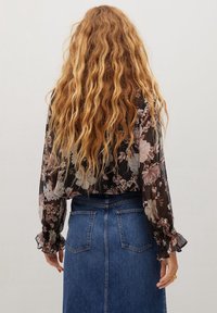 Blouse noire transparente avec des motifs floraux, manches longues bouffantes et poignets volantés, associée à une jupe en denim bleu taille haute.