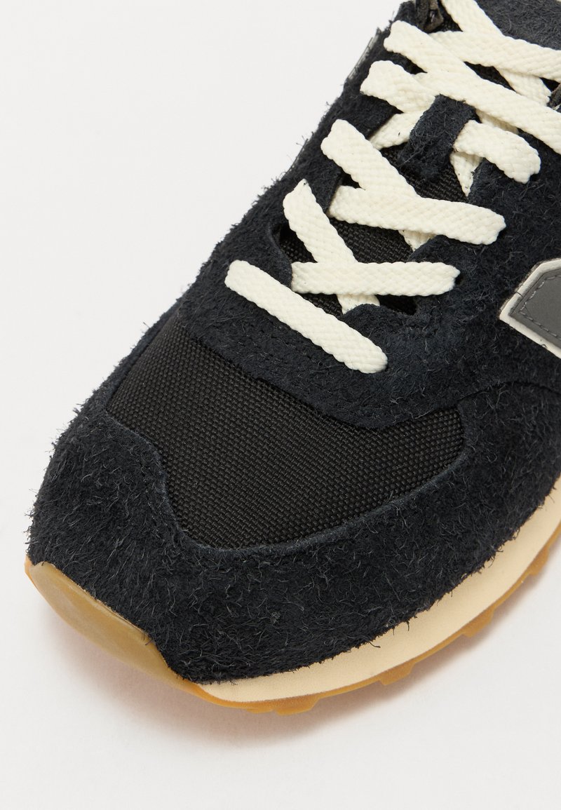 Baskets de sport noires avec un dessus en suède texturé, des sections en mesh, des lacets crème et une semelle en caoutchouc. Détail de marquage gris notable sur le côté.
