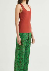 Top aderente rosso con spalline larghe abbinato a pantaloni larghi verdi con motivo floreale su uno sfondo scuro.