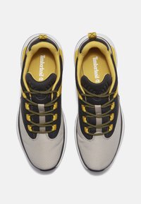 Grijze, zwarte en gele sneakers met een gestructureerde bovenkant, ronde veters en een gevoerde tong. Timberland-logo zichtbaar aan de binnenkant.