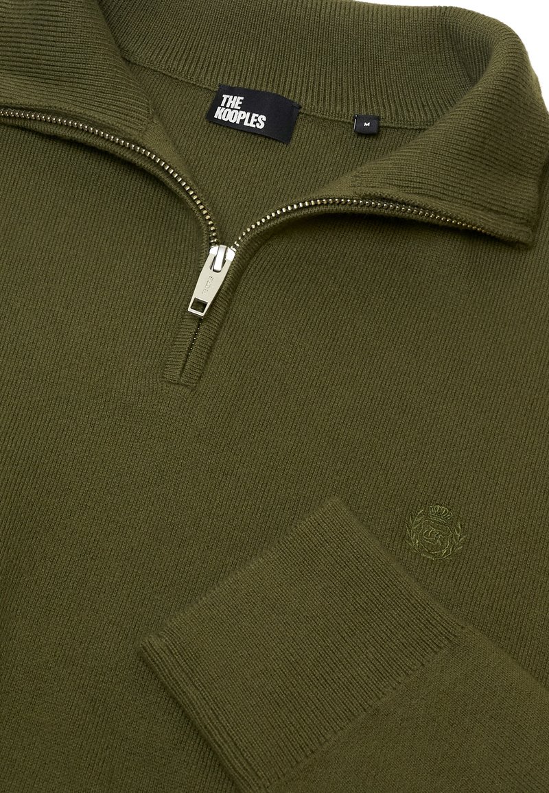 Maglione verde oliva con zip, caratterizzato da una texture a coste, con colletto alto e logo ricamato sul petto. Zip argentata con linguetta brandizzata.