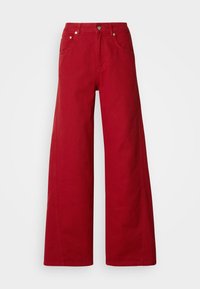 Pantalon rouge à jambes larges avec poches avant, passants pour ceinture et fermeture à bouton, présenté sur un fond gris clair uni.