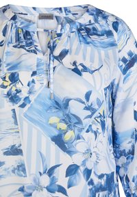 Blue floral blouse with a mix of patterns featuring lemons and scenery. Lightweight fabric, round neckline, and tie detail at the front.