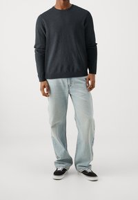 Maglione a maglia grigio scuro con collo a giro, abbinato a jeans larghi di colore blu chiaro e sneaker nere con suola bianca.