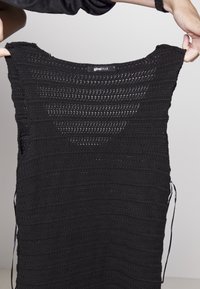 Débardeur en maille noire avec un motif texturé et rayé. Doté d'un col large et de liens sur les côtés pour un ajustement réglable.