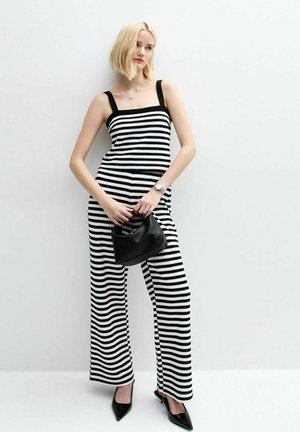 Zwart-wit gestreepte jumpsuit met wijde pijpen, vierkante halslijn en dikke bandjes. Gepaard met een kleine zwarte handtas en puntige hakken.