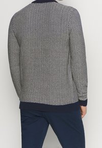 Svetr s námořnickým modrým a bílým vzorem, s žebrovaným límcem a manžetami; texturovaná látka, design na přetažení přes hlavu a jednobarevné detaily na spodním okraji.