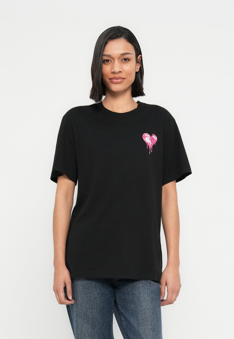 Μαύρο βαμβακερό μπλουζάκι με κοντά μανίκια, που φέρει ένα μικρό ροζ καρδιόγραφο στο αριστερό μέρος του στήθους. Χαλαρή εφαρμογή, απαλή υφή και ίσιο τελείωμα.