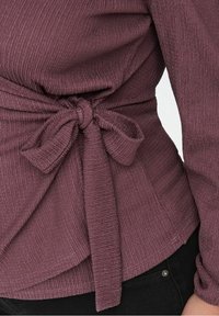 Paarse blouse met textuur en een gestrikte taille, met lange mouwen en een vloeiende silhouet. De stof heeft een subtiel geribd patroon.