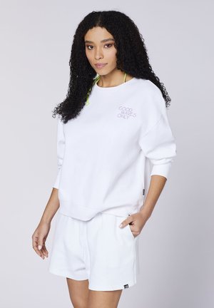 Weißer Sweatshirt mit "GOOD WAVES ONLY" in helllila gestickt. Kombiniert mit passenden weißen Shorts; beide haben einen lässigen und lockeren Schnitt.