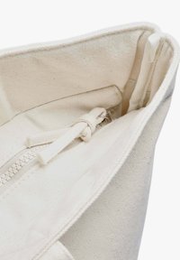 Borsa in tela bianca con finitura testurizzata, dotata di cerniera superiore e tasca interna chiusa con un laccio. Design semplice e funzionale.