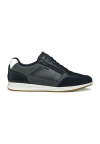 Zapatilla de cuero negro con un panel lateral texturizado, detalle en el talón en blanco y suela de goma en un tono marrón contrastante. Detalle de cremallera en el lateral.