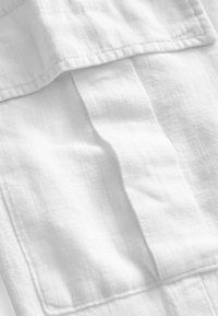 Hvidt linnedstof med en let krøllet tekstur, der har en fold med kantsting detaljer og minimalistisk design.