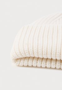 Cream-colored knit beanie with ribbed texture, featuring a soft, warm yarn and folded edge, ideal for winter wear.