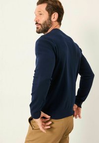 Marineblau gestrickter Pullover mit Rundhalsausschnitt und Rippabschluss, getragen über khakifarbenen Hosen, der eine figurbetonte Silhouette und lange Ärmel präsentiert.