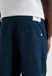 Granatowe szorty z fakturowanej tkaniny, z elastycznym paskiem w talii i dwiema tylnymi kieszeniami. Biała metka z logo powyżej pasa.