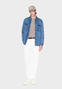 Camicia di denim, t-shirt beige, pantaloni bianchi a gamba larga, sneakers bianche, cappellino color cammello. Caratteristiche principali includono tasche e un design texturizzato della camicia.