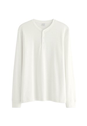 Valkoinen pitkähiha-ristikko Henley-paita, jossa on pyöreä kaula-aukko ja kolme nappia edessä.