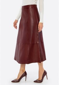 Bordeauxrode leren midi-rok met een gladde textuur en een A-lijn snit, voorzien van subtiele naden en een hoog getailleerd ontwerp. Gecombineerd met bruine hakken.