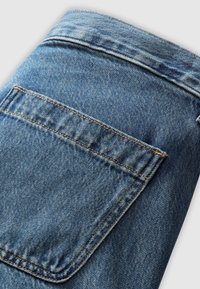 Tissu en denim bleu montrant une poche arrière avec une couture orange sur un jean classique, plié sur un fond blanc.