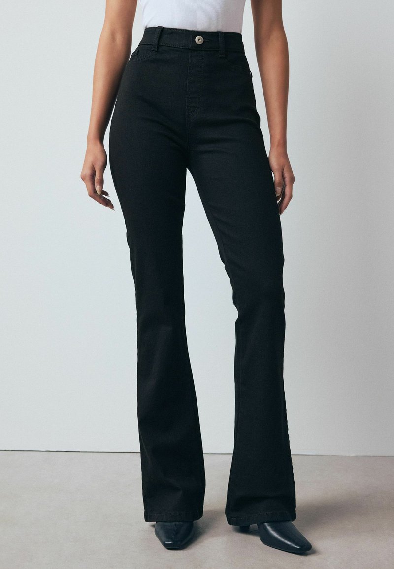 Black high-waisted flared jeans made of stretchy denim, featuring a front pocket and a button closure, with a smooth, textured finish.