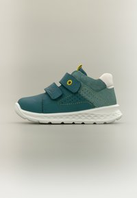 Παιδικό αθλητικό παπούτσι σε τιρκουάζ με λευκή σόλα, δύο ρυθμιζόμενους ιμάντες Velcro, κίτρινη ραφή και επένδυση στον αστράγαλο.