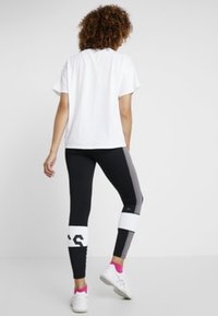 T-shirt bianco a maniche corte abbinato a leggings neri con blocchi di colore grigi e bianchi, dettagli neri e calzature rosa.