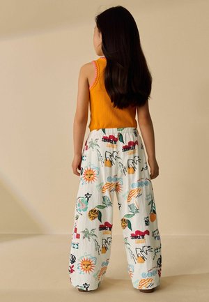 Enfant aux longs cheveux foncés portant un haut orange sans manches et un pantalon blanc à jambes larges avec des imprimés colorés sur le thème de l'été, de dos.