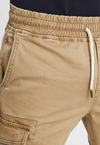 Khakifarbene Cargoshorts mit elastischem Bund, Kordelzug und Seitentaschen. Der Stoff hat eine glatte Textur und einen dezenten Glanz.
