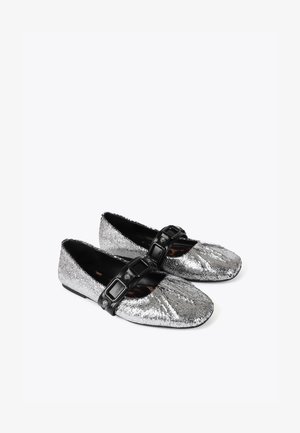 Srebrne baleriny z metaliczną teksturą, okrągłym noskiem i czarnym paskiem z klamrą na wierzchu stopy. Płaska, elastyczna podeszwa.